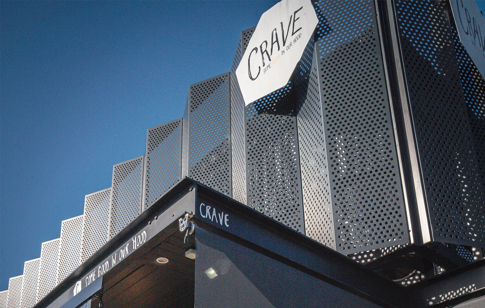 Close-up of angular perforated metal cladding on building exterior with signage, blue sky above