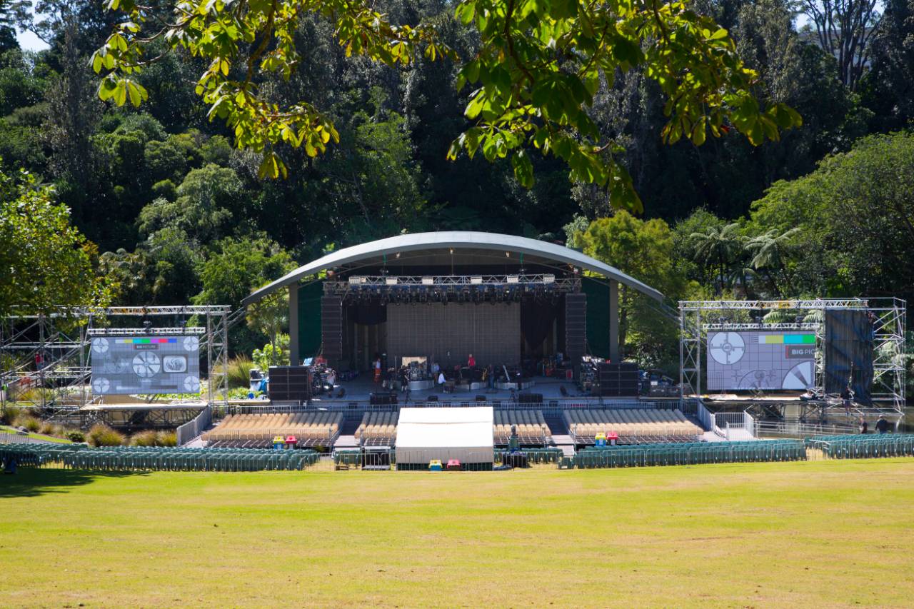 Outdoor amphitheatre with covered stage, seating, and large screens in parkland