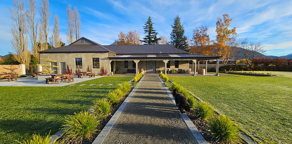 Single-storey rendered venue building with covered veranda, gardens, and mountain backdrop
