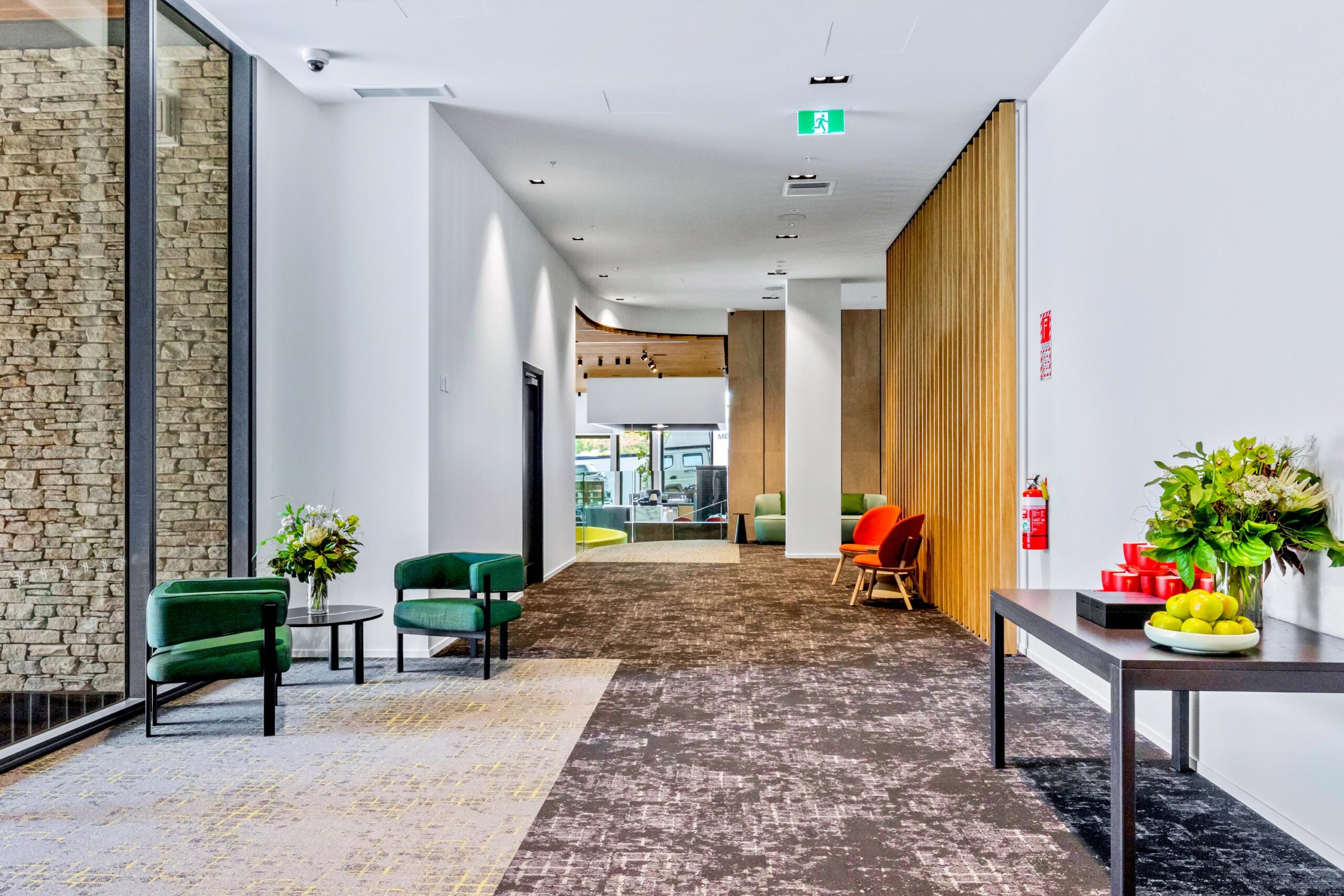 Contemporary foyer corridor with stone wall, timber slat partition, and colourful lounge chairs