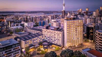 Aerial dusk view of large multi-storey city hotel with illuminated tower and surrounding urban skyline