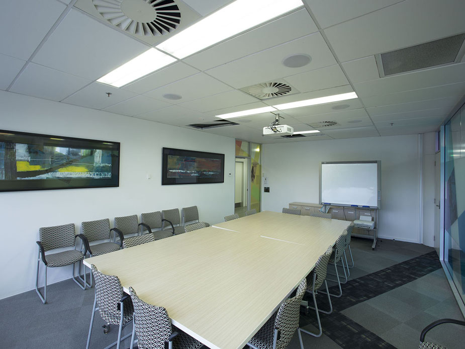 Meeting room with long timber table, patterned chairs, projector, and framed artworks