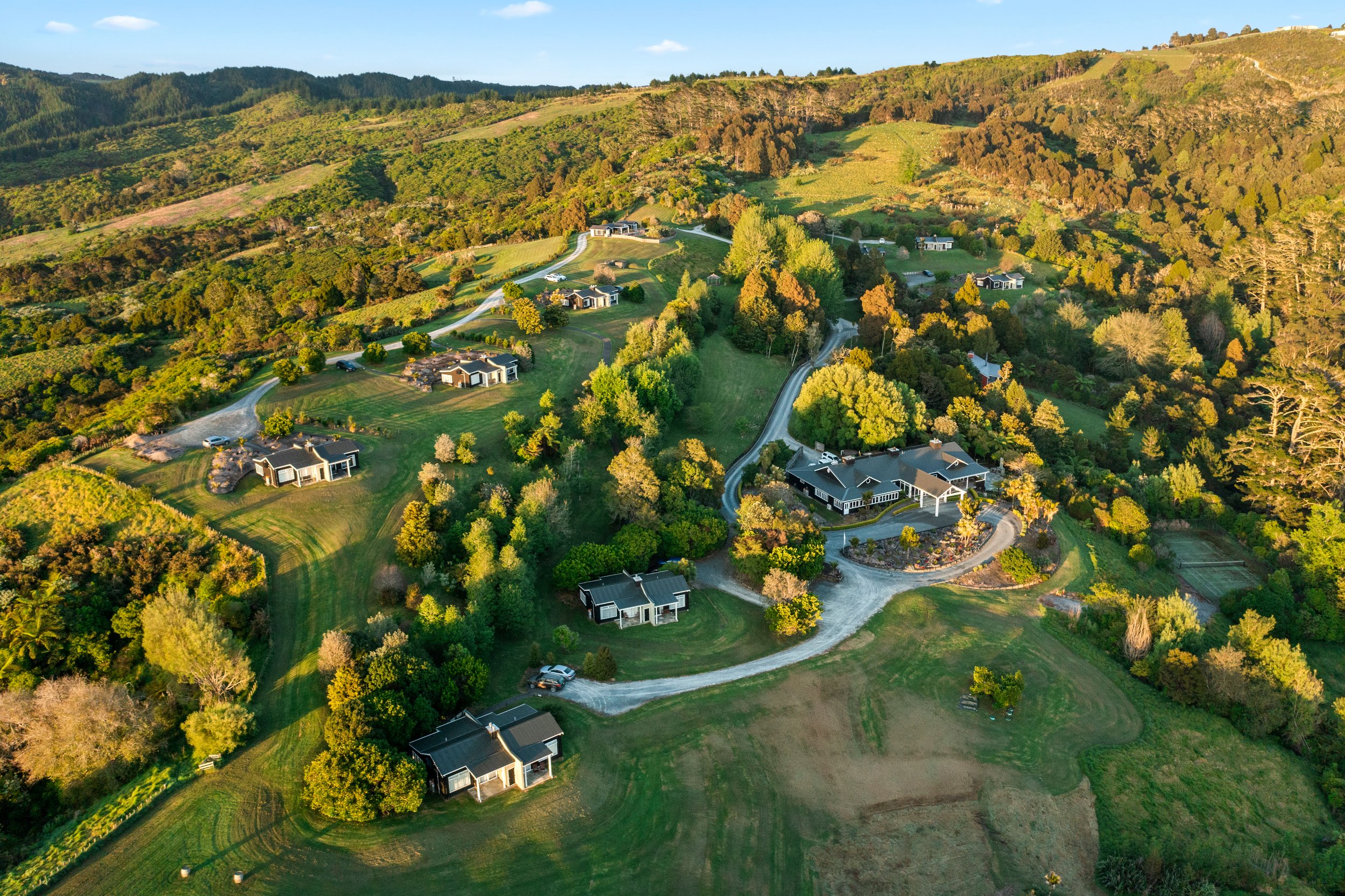 Aerial view of scattered dark-roof lodges across rolling green hills and woodland