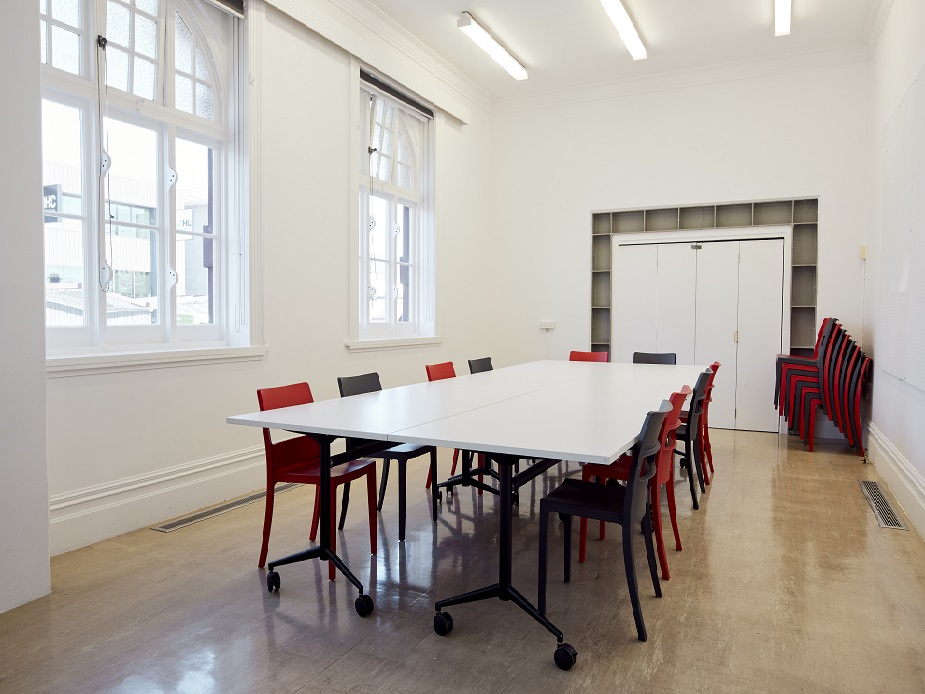 White meeting room with large windows, long folding table, red and dark chairs, polished floor