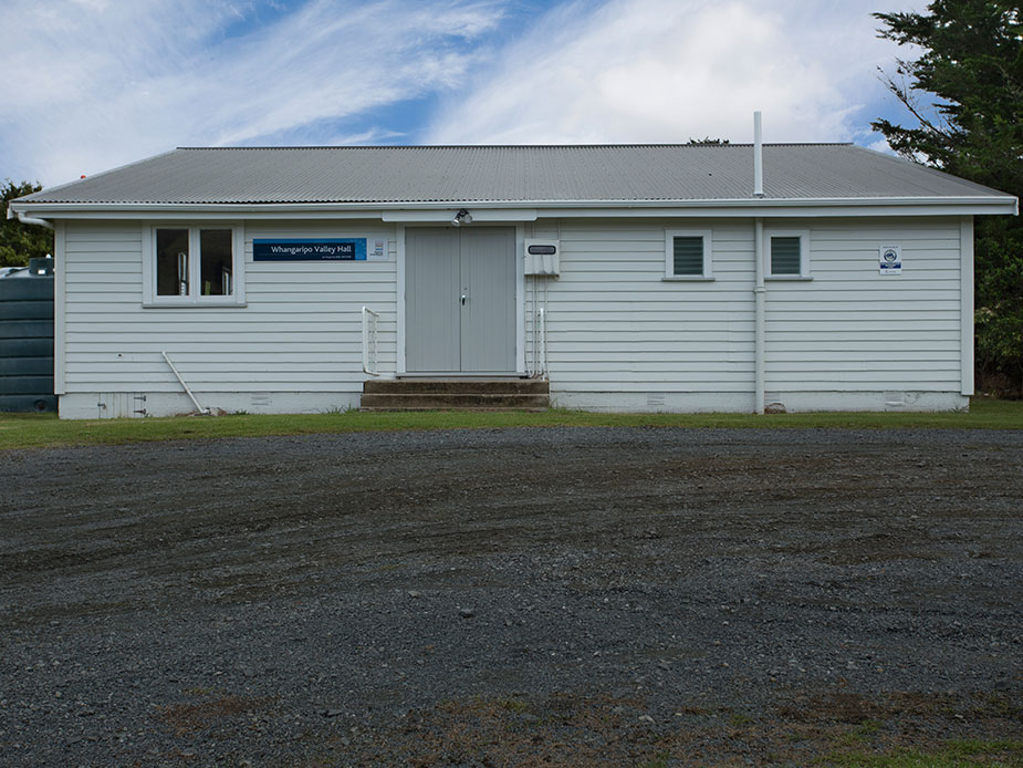 White weatherboard hall with grey iron roof and gravel car park