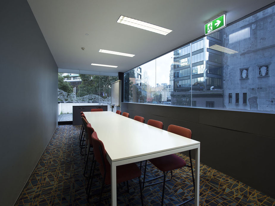 Narrow meeting room with long white table, red chairs and floor-to-ceiling windows