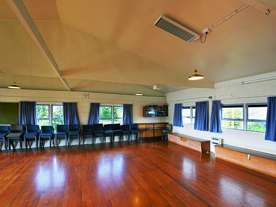 Timber-floored hall with rows of chairs, drape curtains and raked ceiling