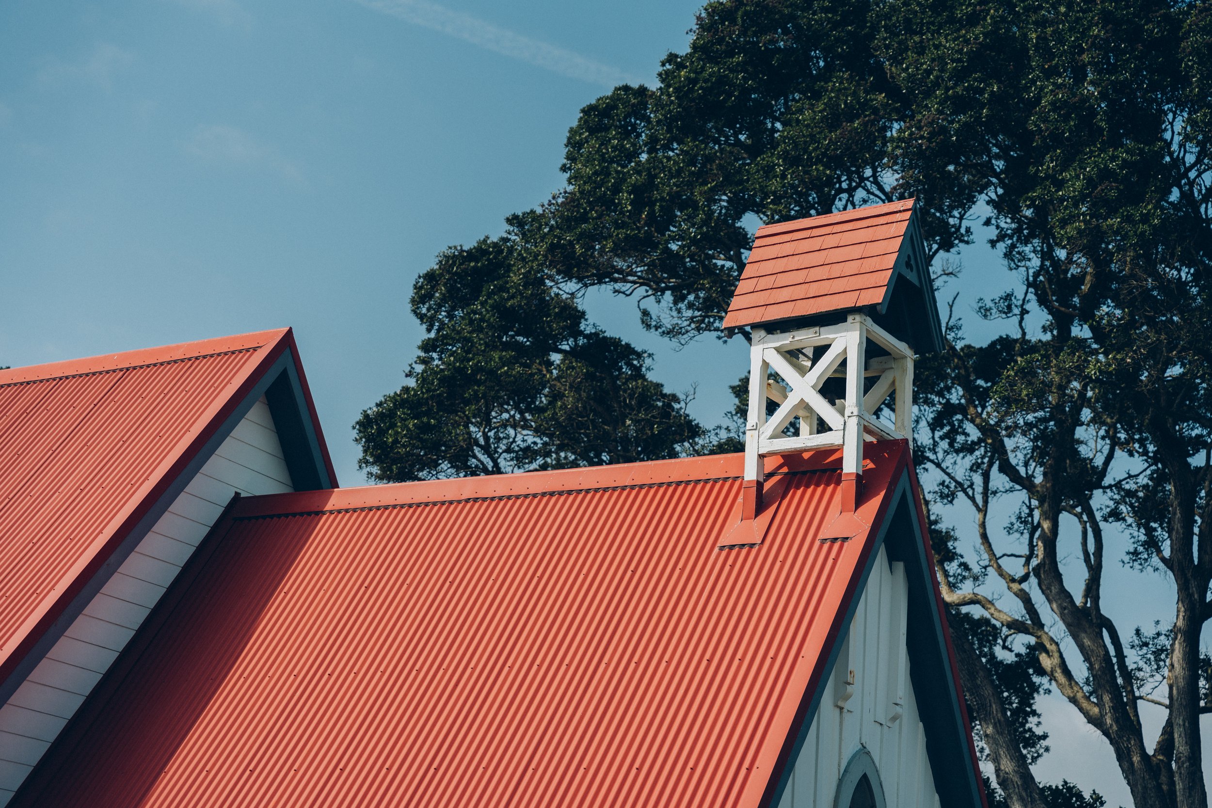 Close-up of timber church roofline with red corrugated iron and small bell tower against blue sky