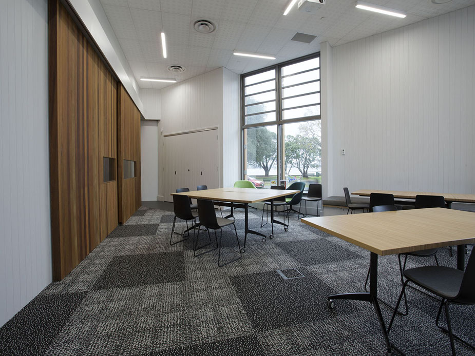 Meeting room with timber feature wall, light wood tables and dark chairs, tall windows, whiteboard