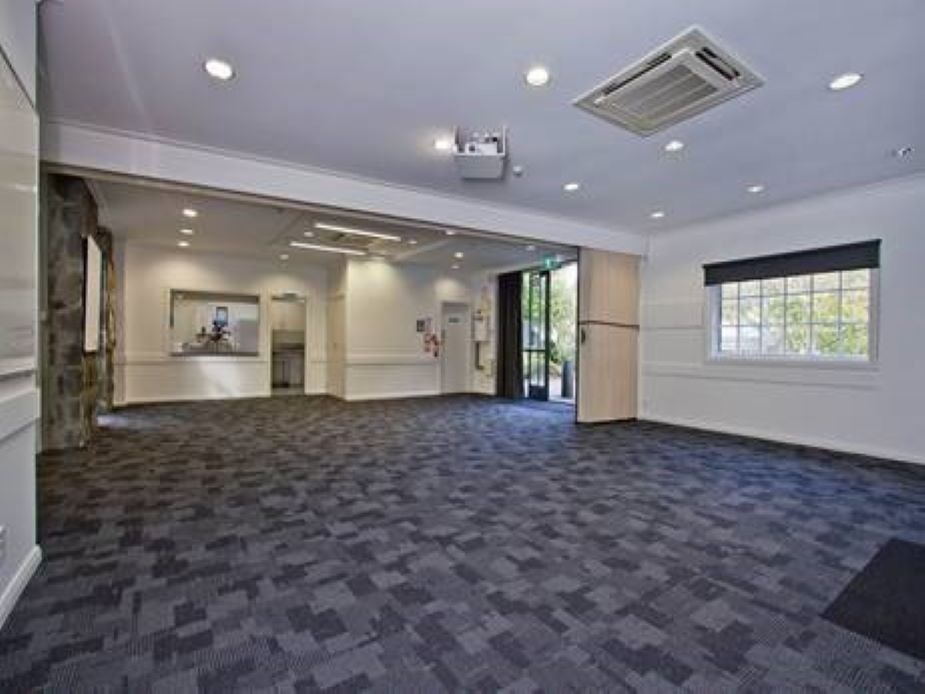 Open carpeted function room with projector and servery counter, folding partition visible