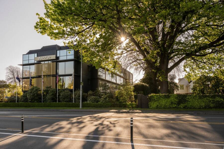 Dark multi-storey building with vertical timber screens, large trees framing the street frontage
