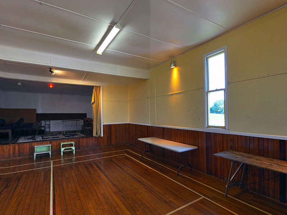 Plain rectangular hall with timber wainscoting, polished floorboards, and fluorescent lighting