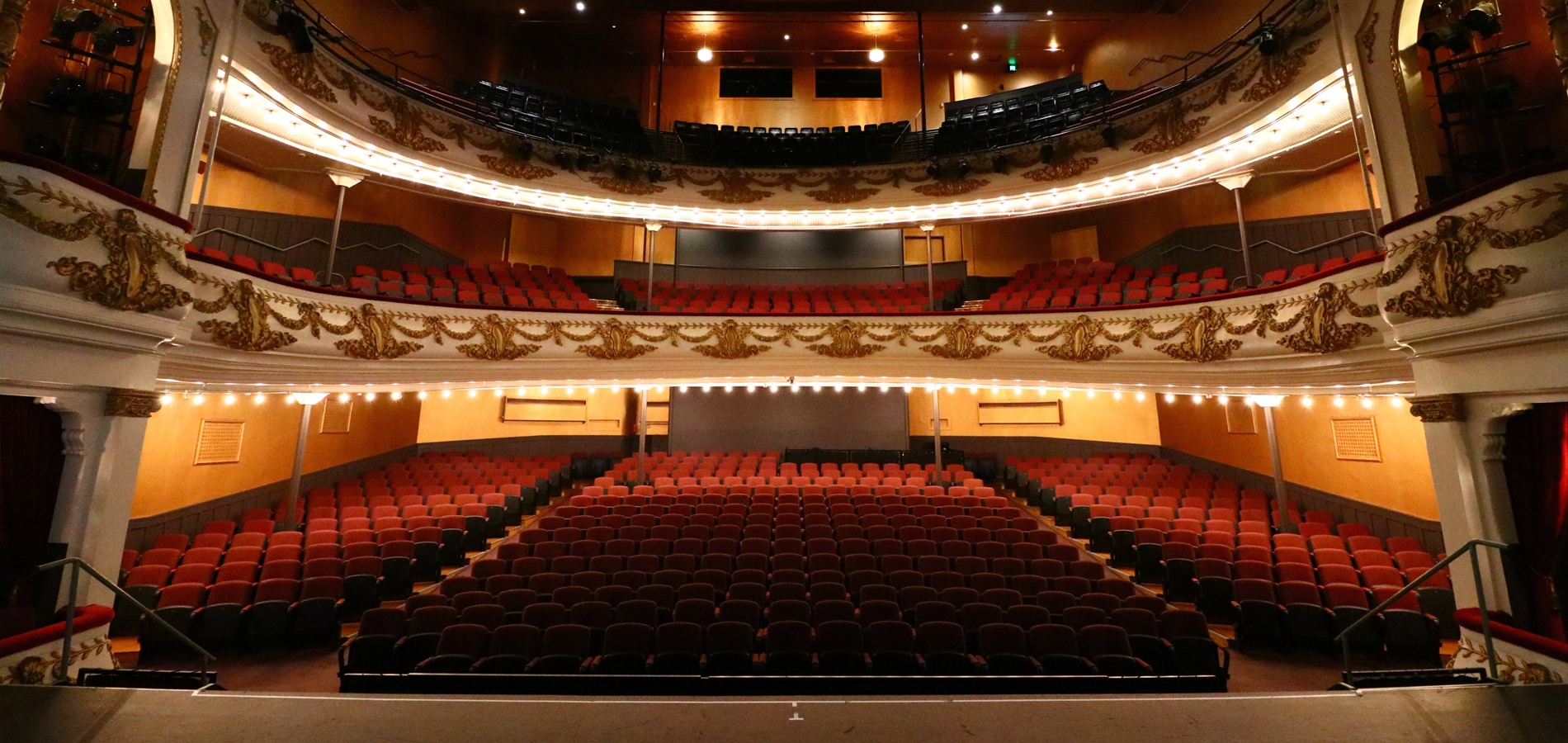Ornate theatre auditorium with red seating, balcony and decorative plasterwork