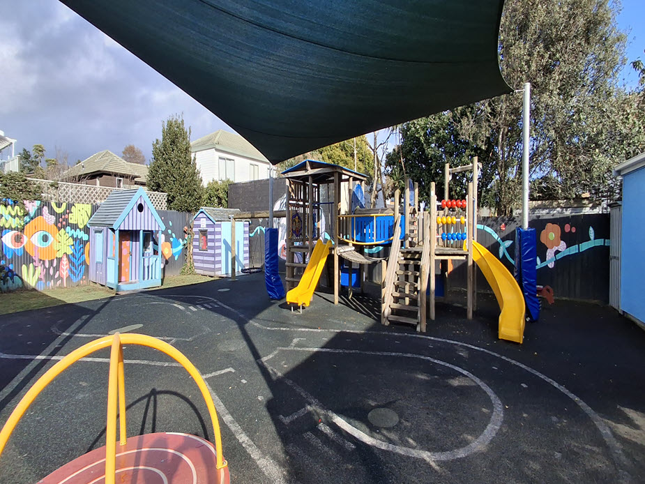 Fenced playground with slides, climbing frames and shade sail