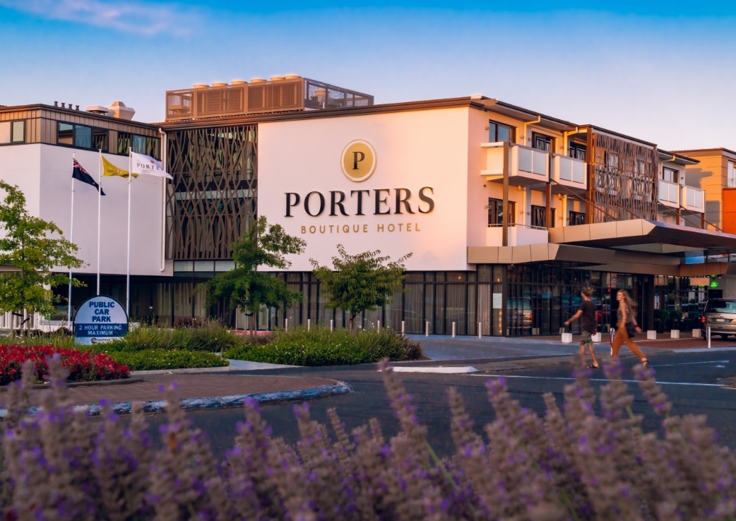 Contemporary multi-storey hotel with timber-screen facade, signage and landscaped forecourt at dusk