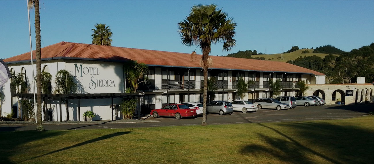 Two-storey motel building with parking area and palm trees in foreground