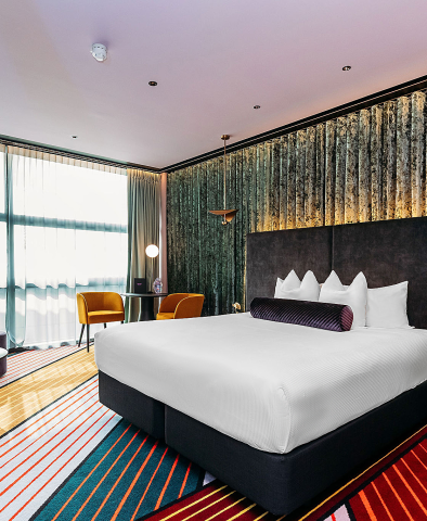 Hotel room with large bed, teal-toned feature wall and yellow accent chairs