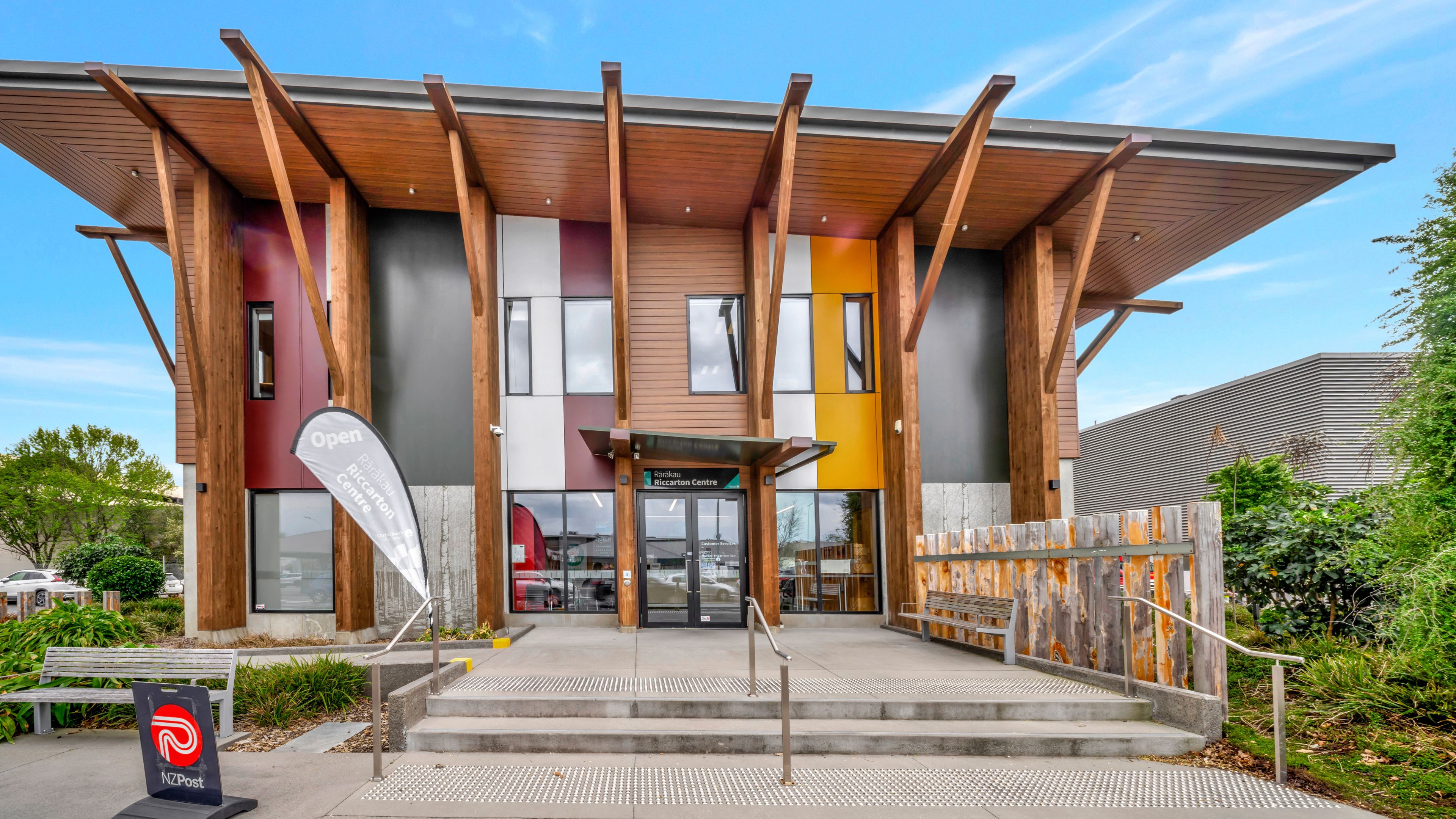 Two-storey community centre exterior with angled timber columns, coloured cladding panels, and covered entry