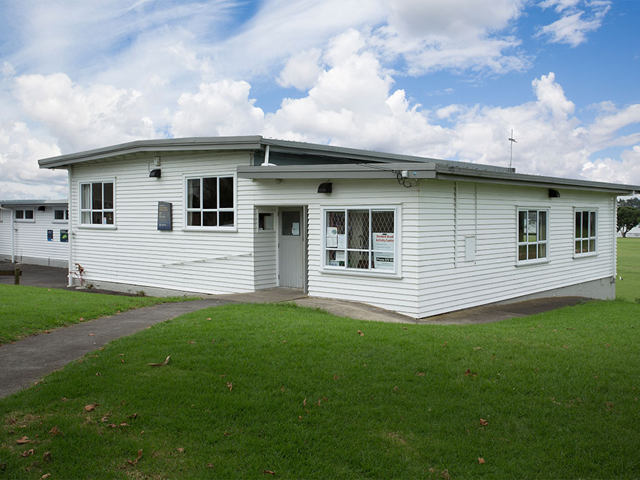 Single-storey white weatherboard community building with lawn