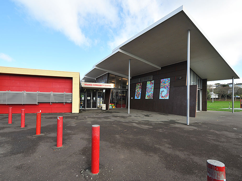 Mid-century community centre with flat canopy roof, dark cladding, and colourful artwork panels